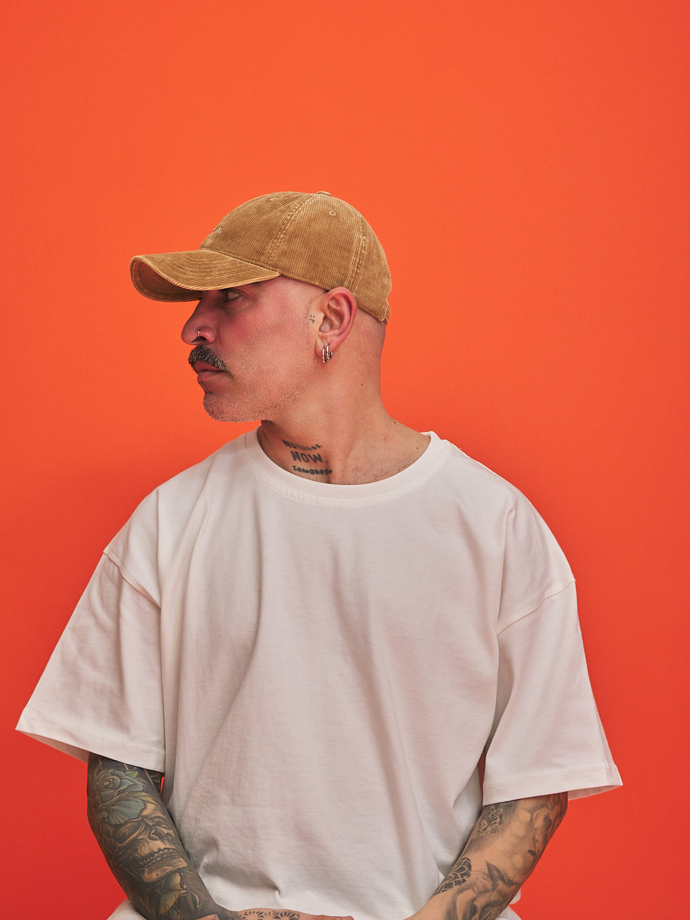 Person wearing a camel cap and white t-shirt against an orange background