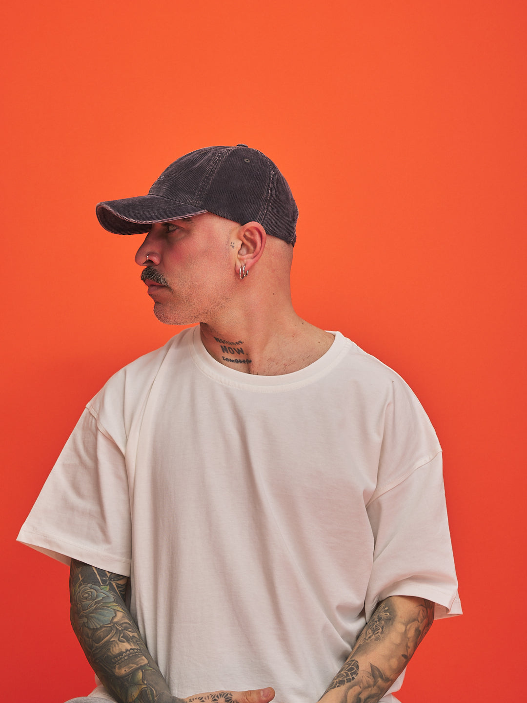 Person wearing a white t-shirt and dark cap against an orange background