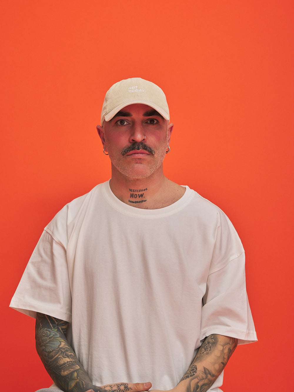 Man wearing a cream cap and white t-shirt against an orange background
