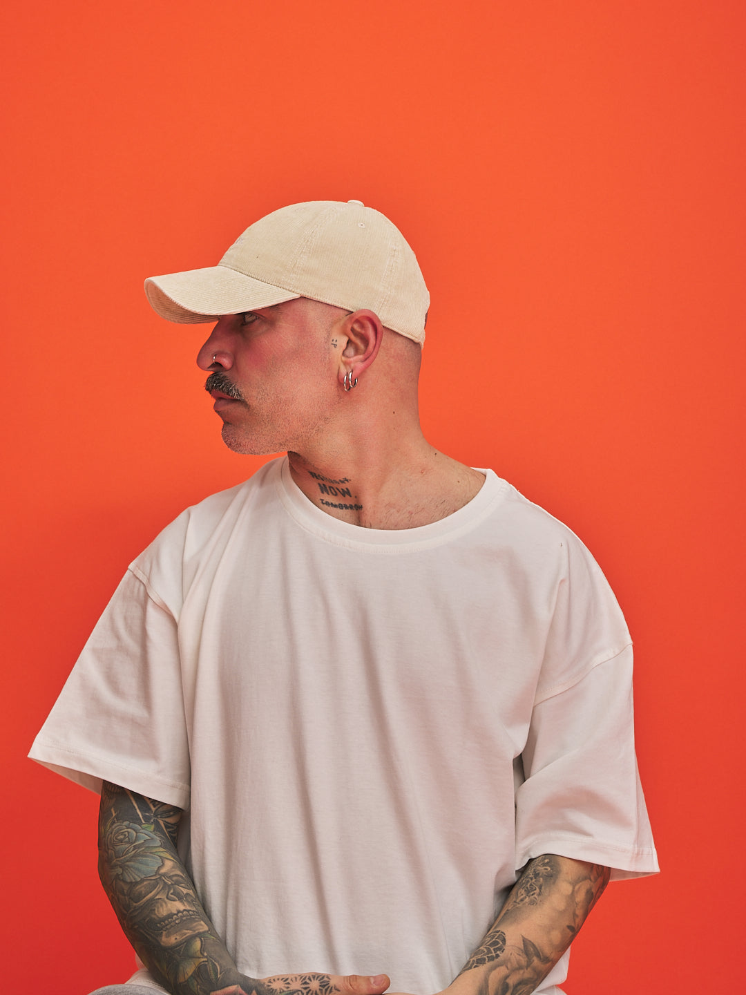 Person wearing a cream cap and white t-shirt against an orange background