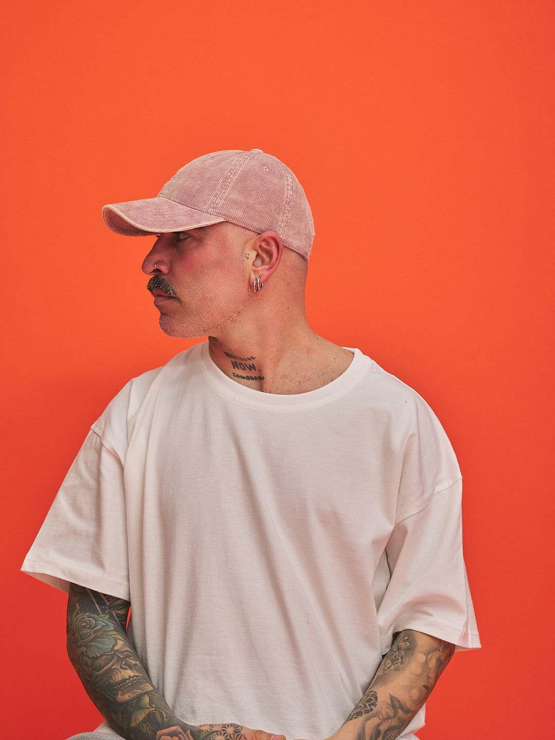 Person wearing a white t-shirt and pink cap against an orange background