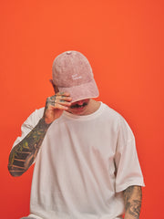 Person wearing a pink cap with a logo on an orange background