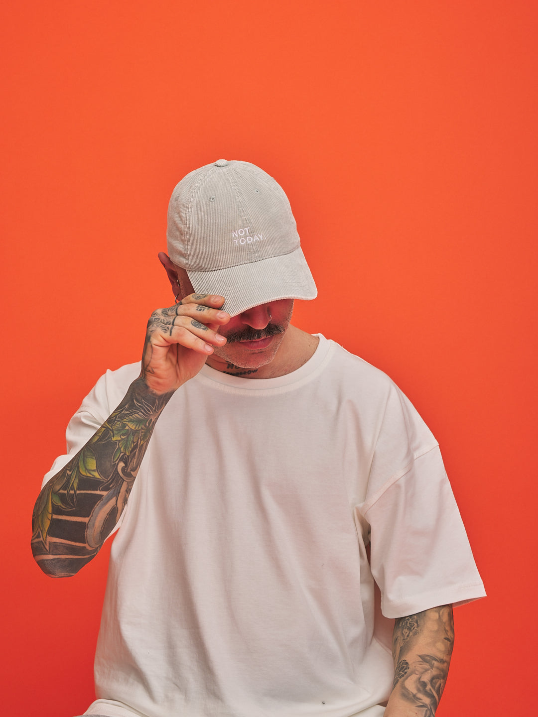 Person wearing a light gray cap and white t-shirt against an orange background