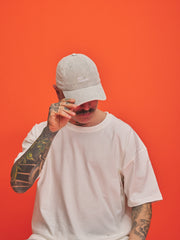 Person wearing a light gray cap and white t-shirt against an orange background