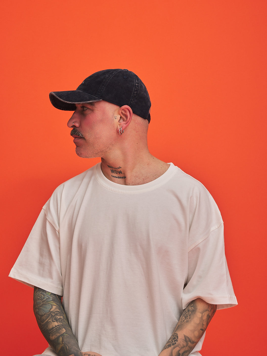 Person wearing a navy cap and white t-shirt against an orange background