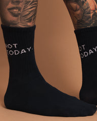 Side look of navy socks with 'Not Today' text worn by a person with tattoos on a brown background