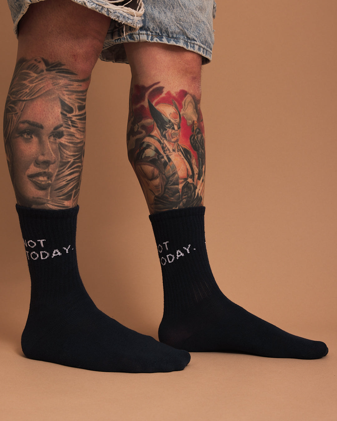 Navy socks with 'Not Today' text worn by a person with tattoos on a beige background