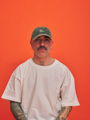Man wearing a green cap and white t-shirt against an orange background