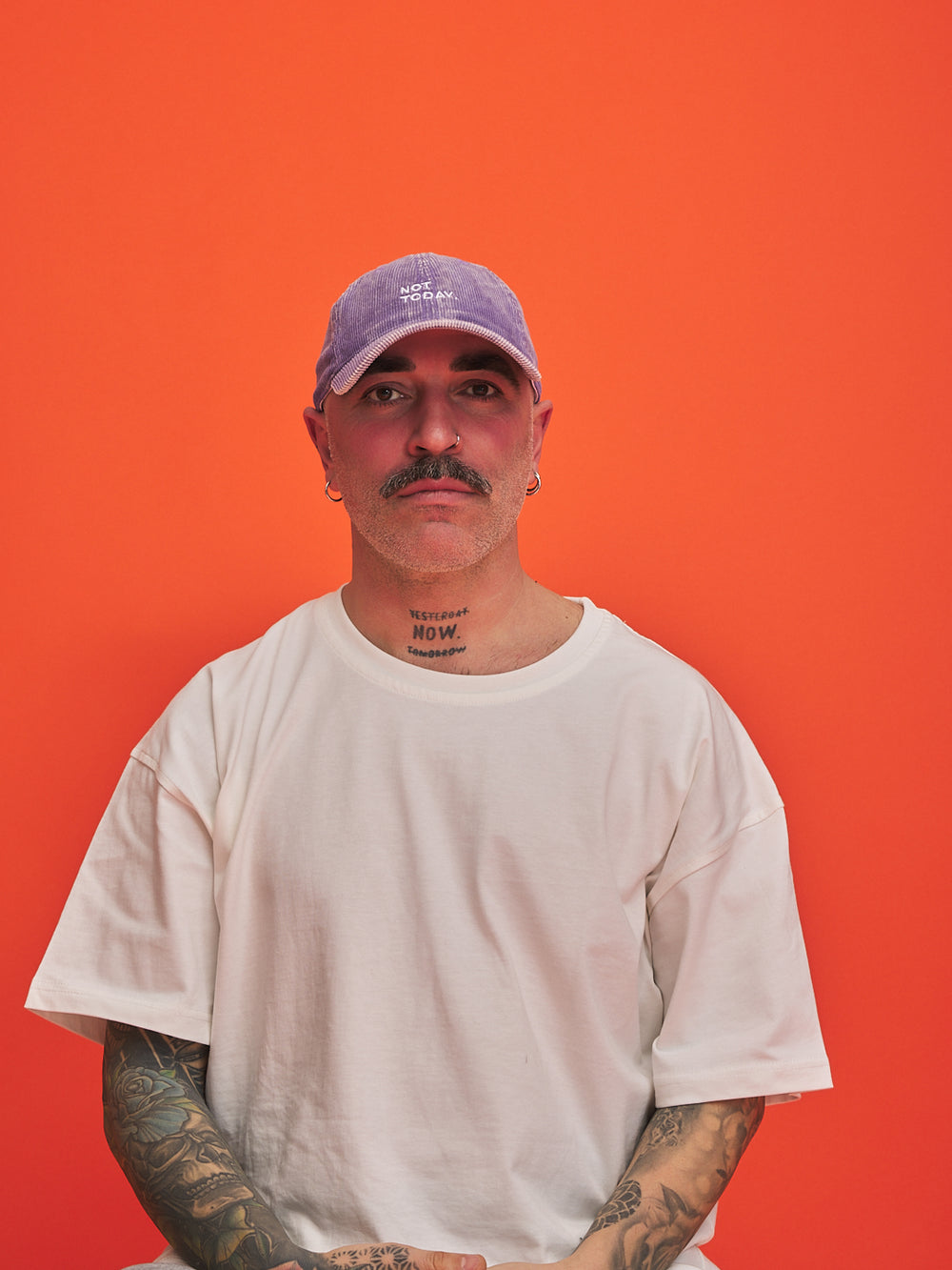 Person wearing a white t-shirt and purple cap against an orange background