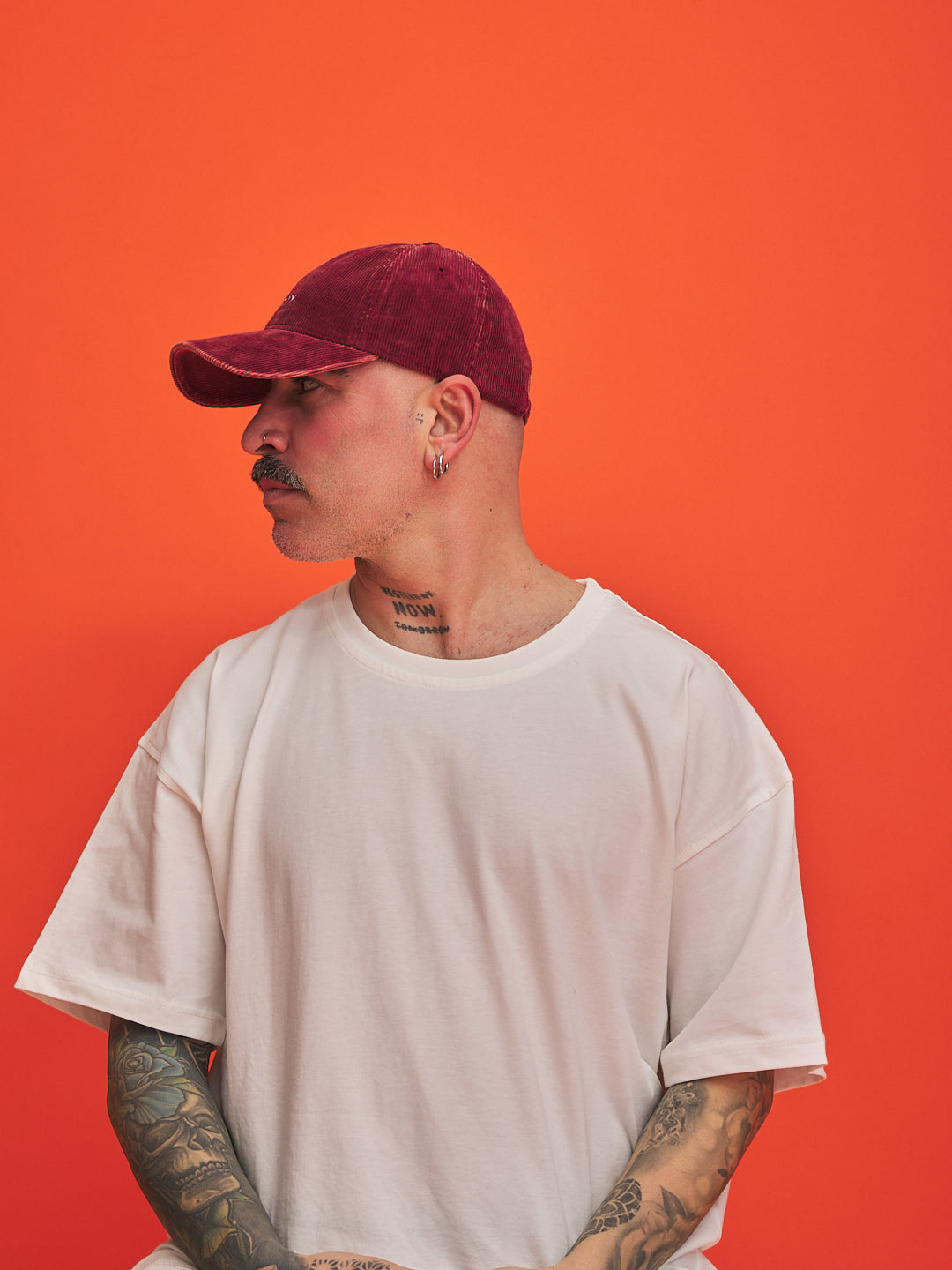 Person wearing a red cap and white t-shirt against an orange background