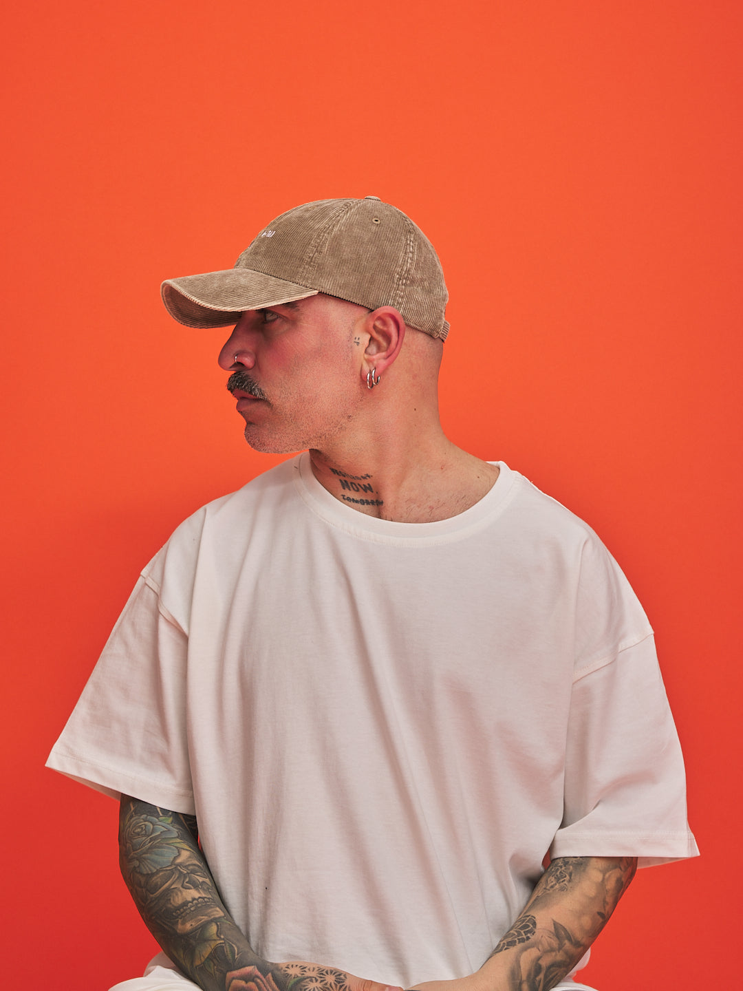 Person wearing a beige cap and white t-shirt against an orange background