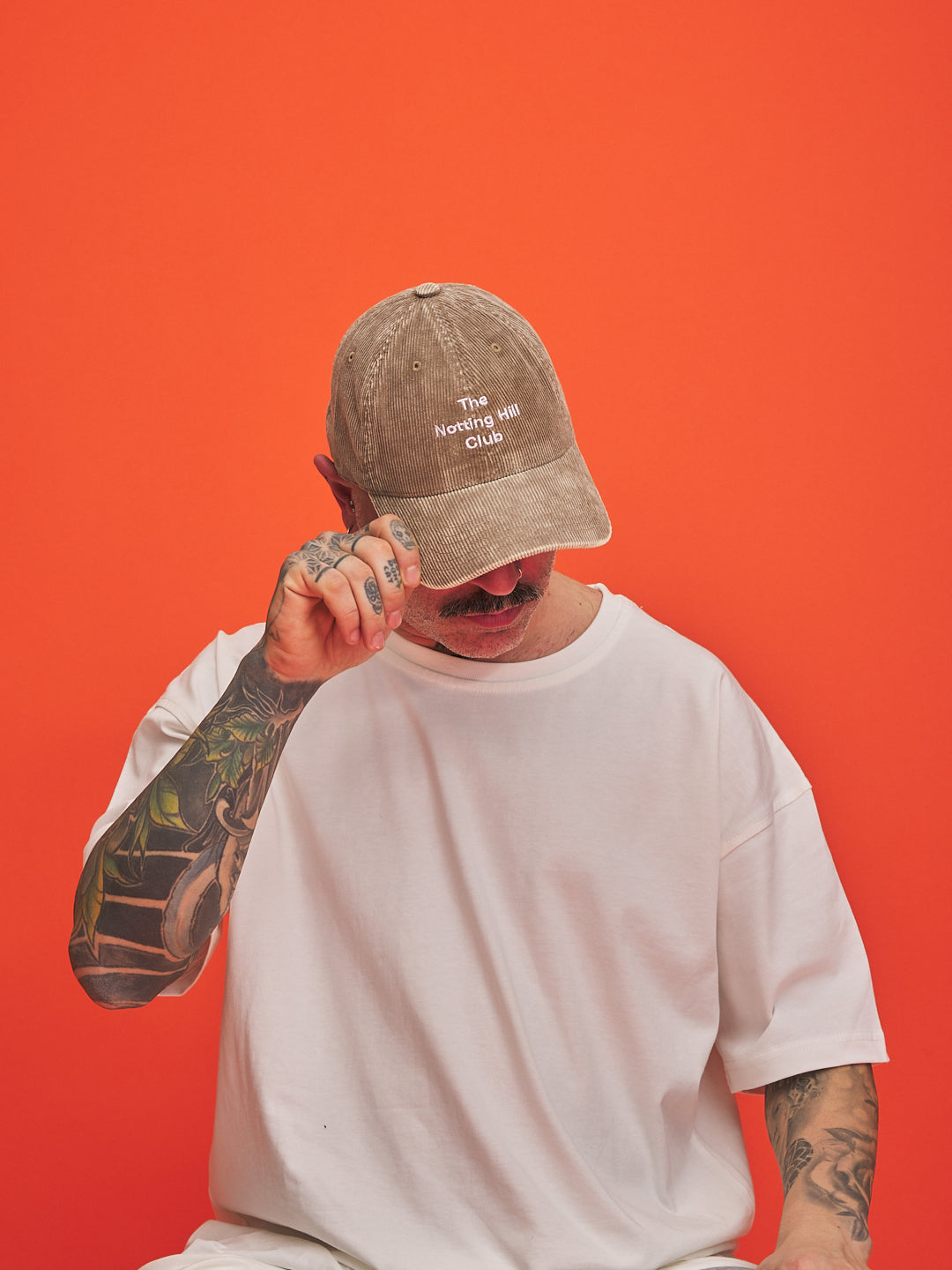 Person wearing a cap with text, holding a mustache against an orange background
