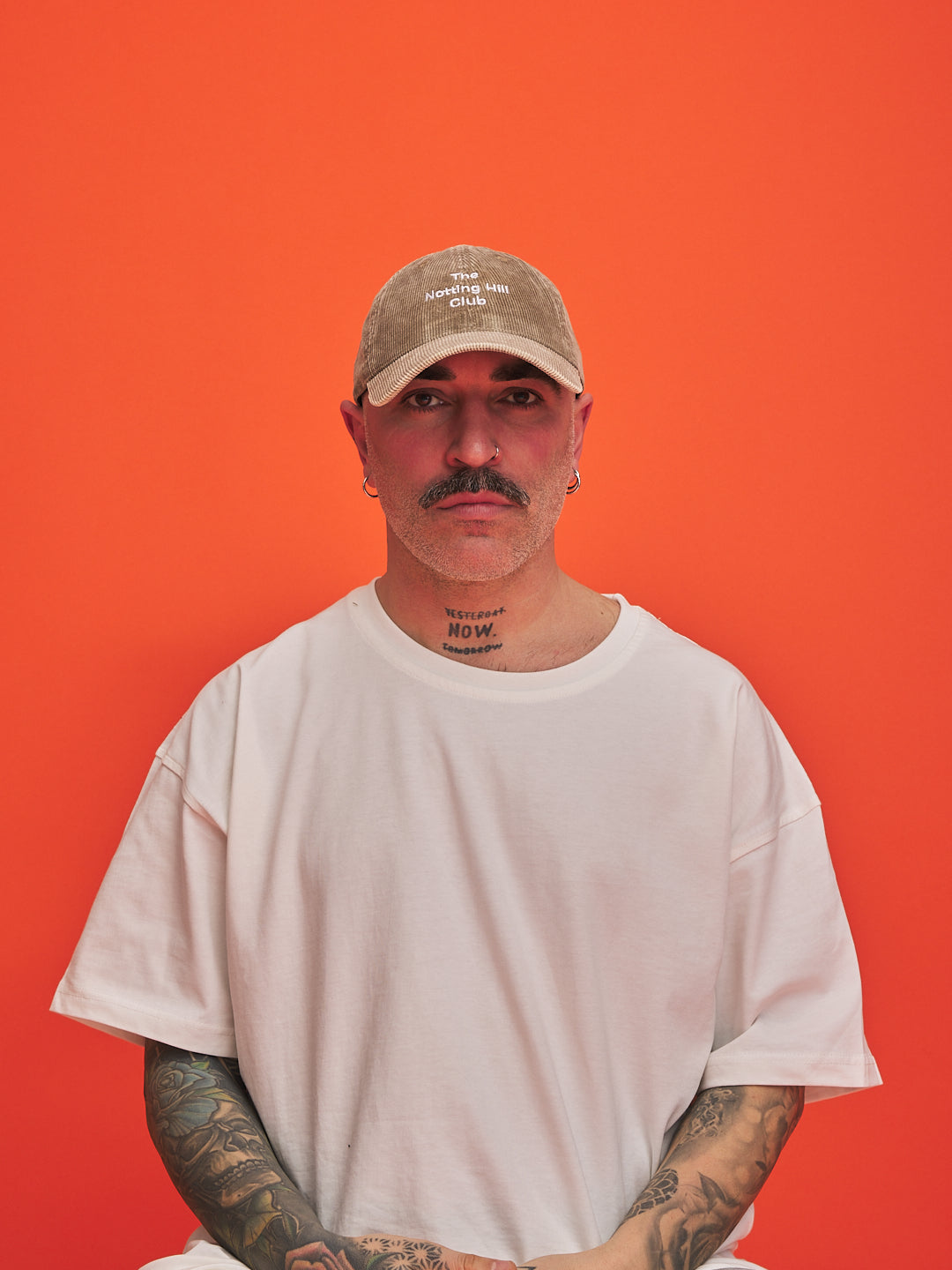 Man wearing a beige cap and white t-shirt against an orange background