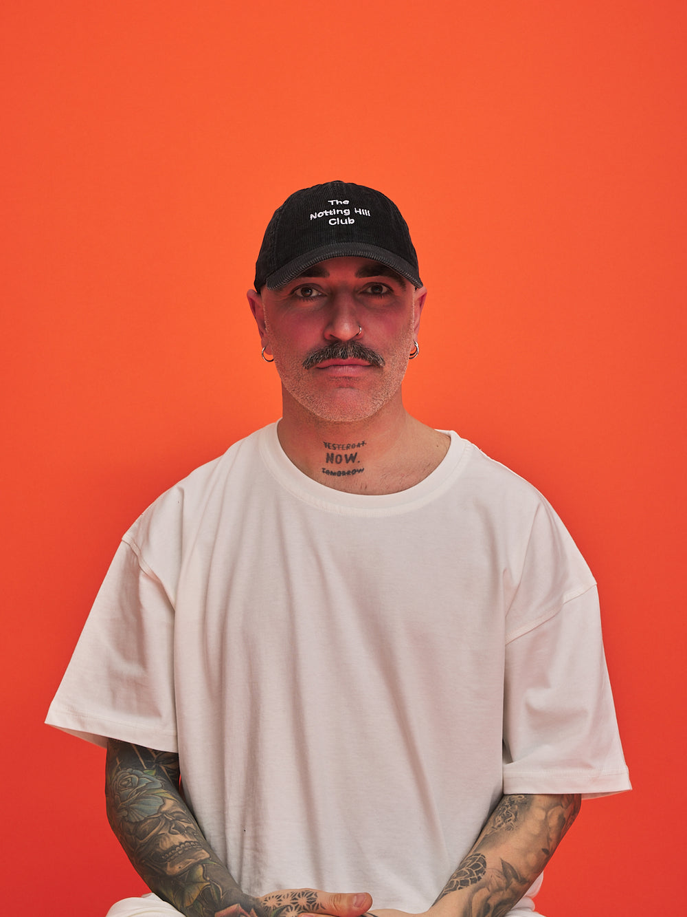 Man wearing a black cap and white t-shirt against an orange background