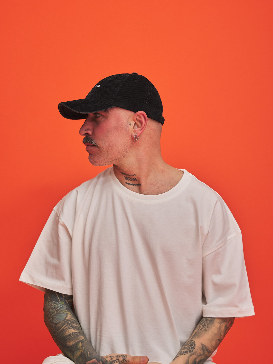 Man wearing a black cap and white t-shirt against an orange background