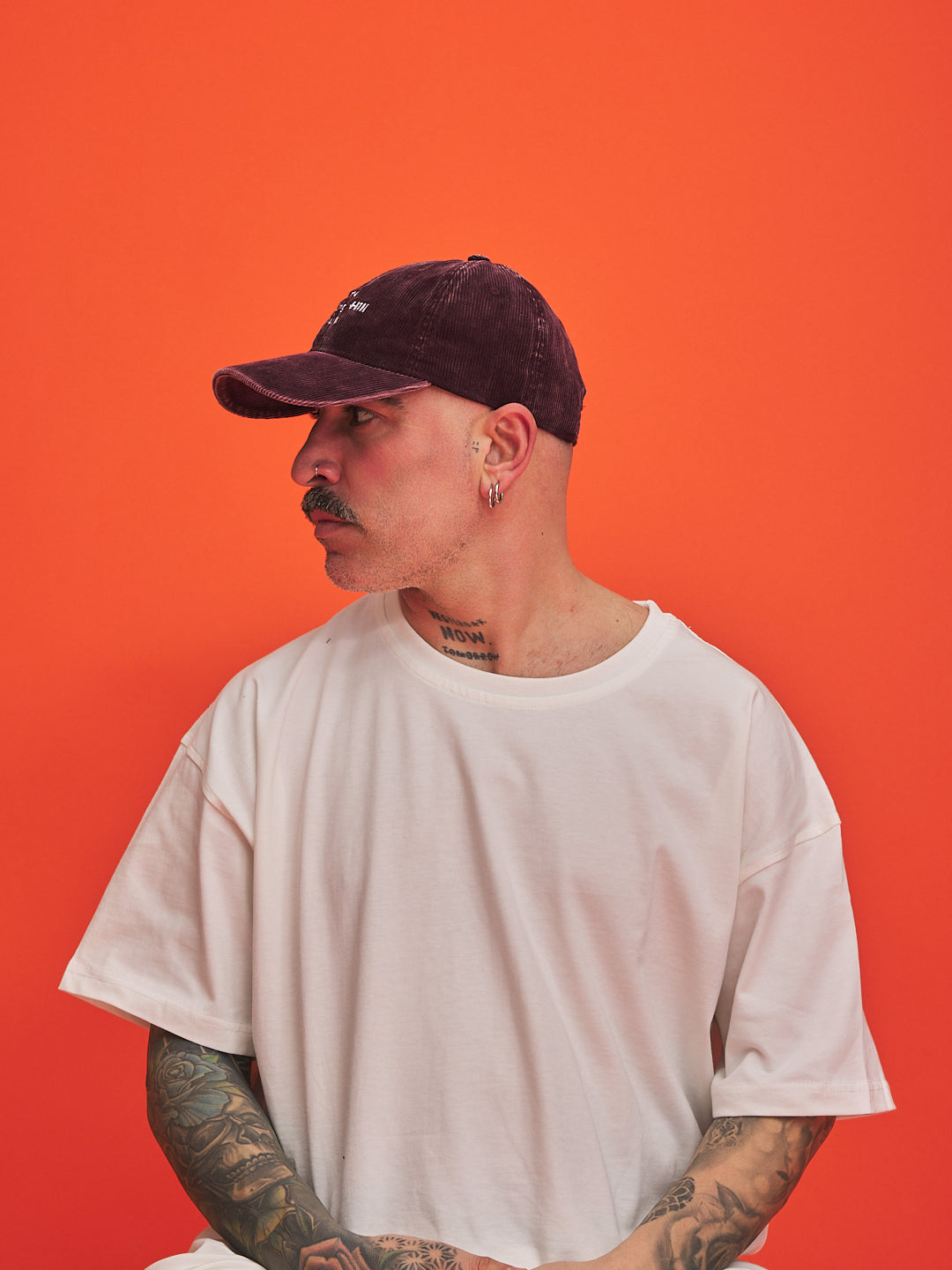 Man wearing a white t-shirt and dark cap against an orange background