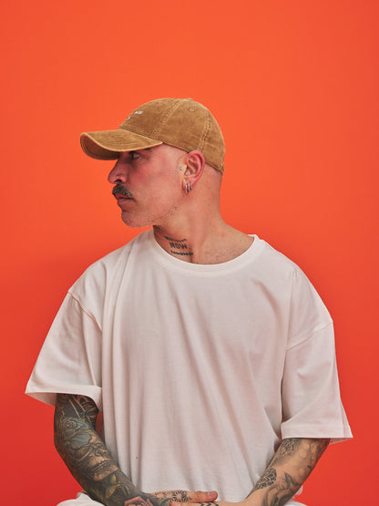 Man wearing a camel cap and white t-shirt against an orange background