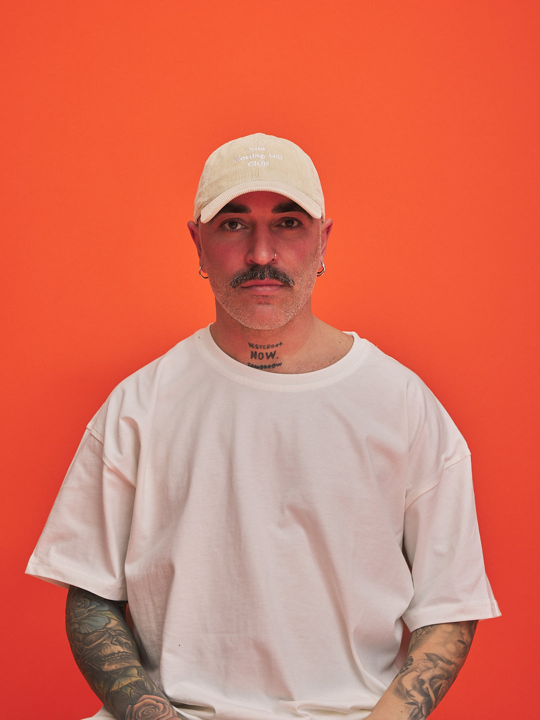 Man wearing a cream cap and t-shirt against an orange background