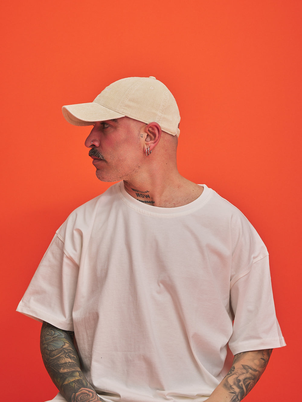Man wearing a cream cap and white t-shirt against an orange background