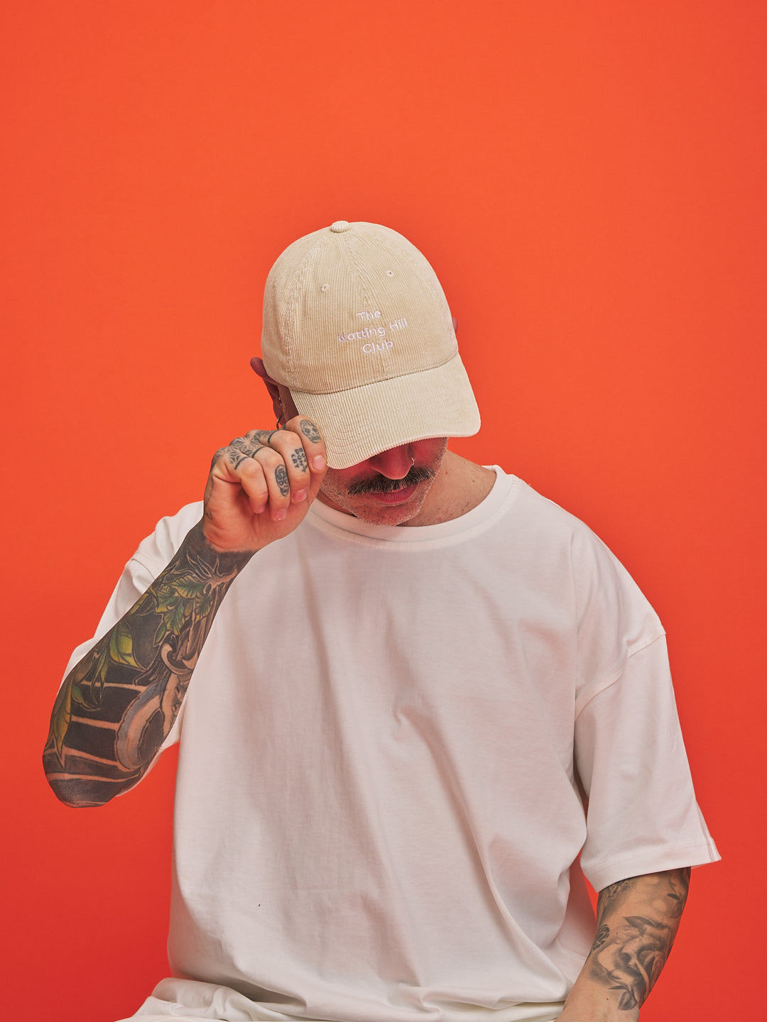 Person wearing a cream cap and white t-shirt against an orange background