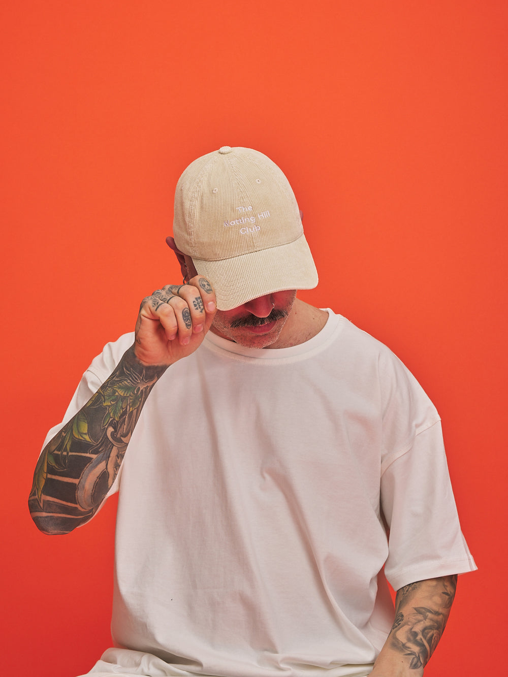 Person wearing a cream cap and white t-shirt against an orange background