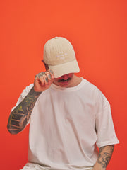 Person wearing a cream cap and white t-shirt against an orange background