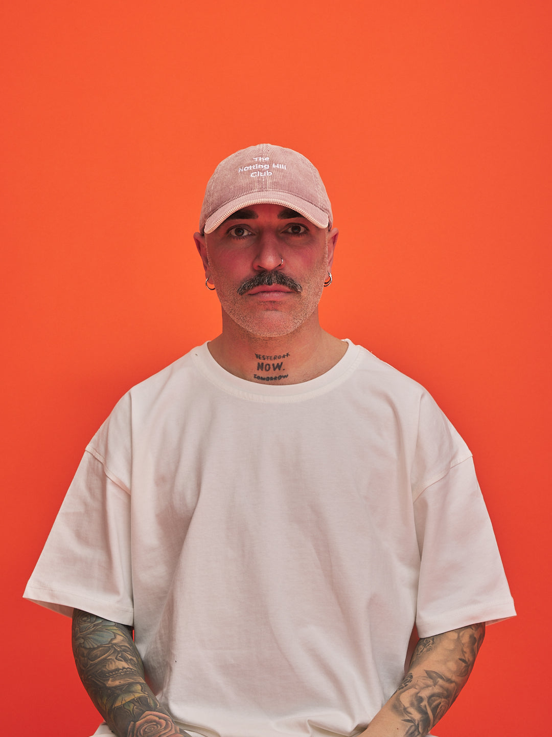 Man wearing a pink cap and white t-shirt against an orange background