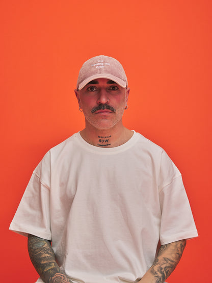 Man wearing a pink cap and white t-shirt against an orange background