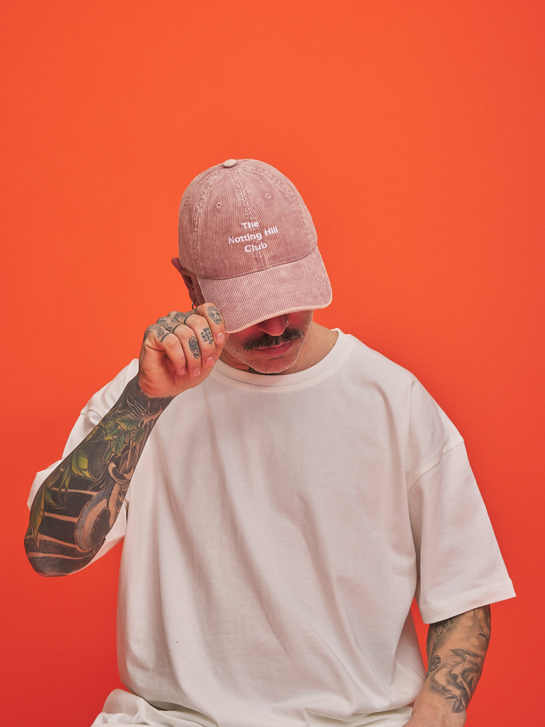 Person wearing a pink cap and white t-shirt against an orange background