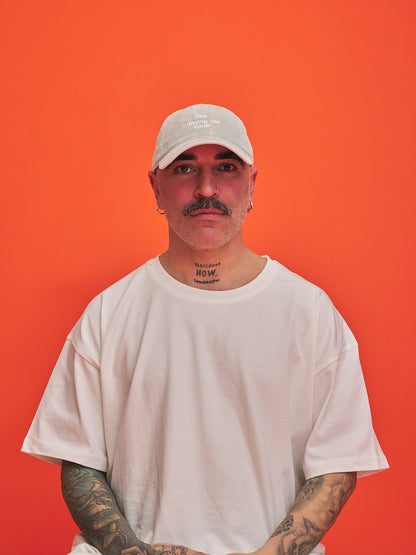 Man wearing a light grey cap and t-shirt against an orange background