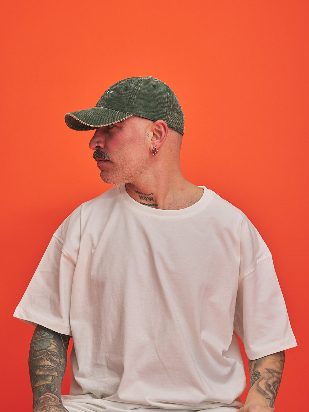 Person wearing a green cap and white t-shirt against an orange background