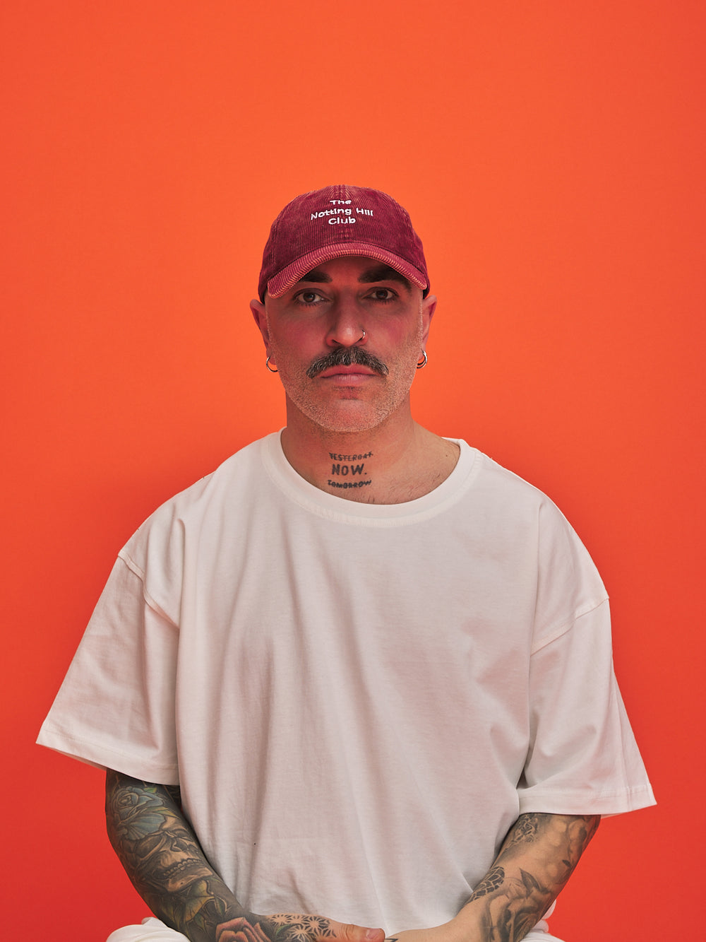 Person wearing a red cap and white t-shirt against an orange background