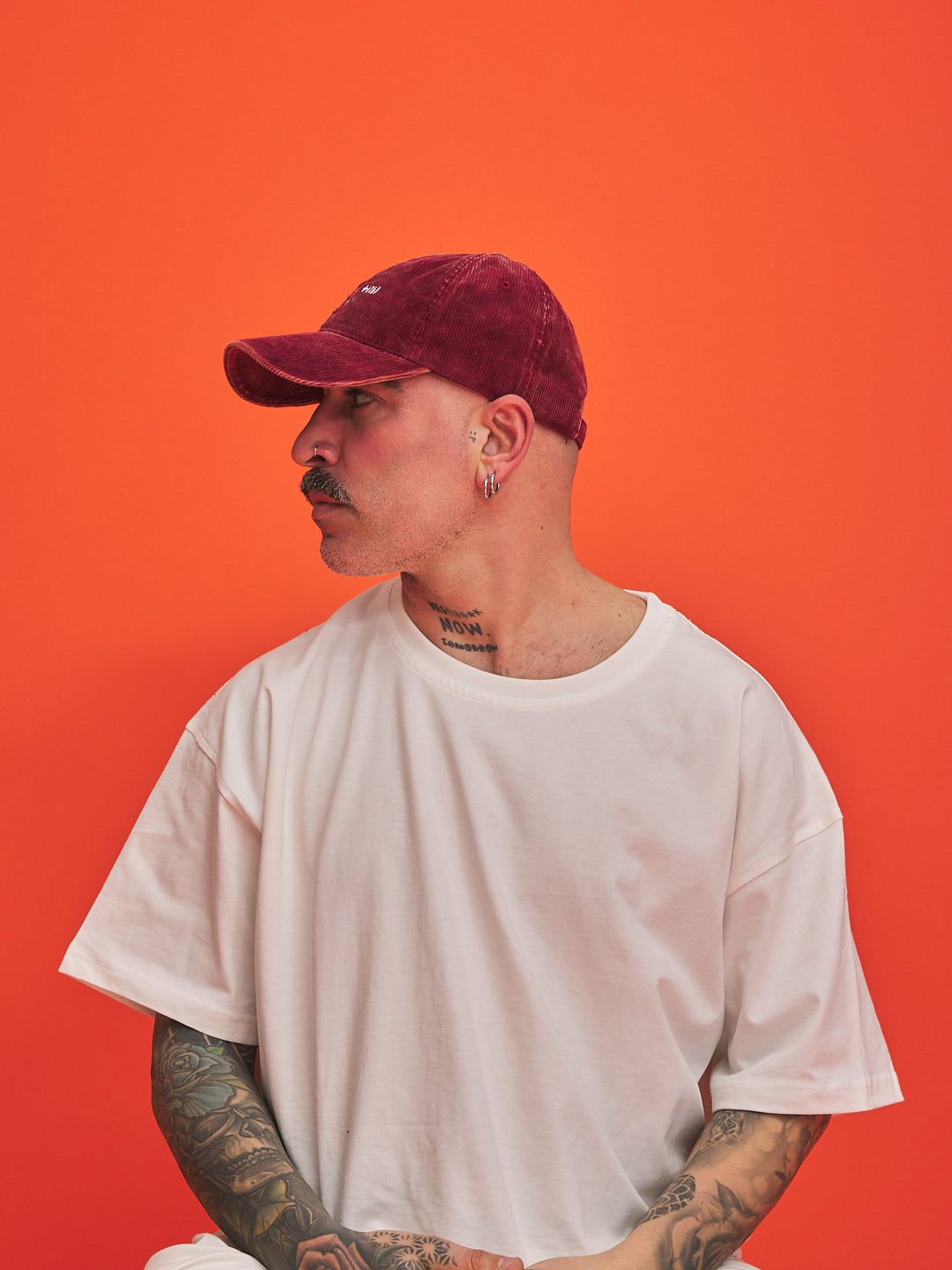 Man wearing a white t-shirt and red cap against an orange background