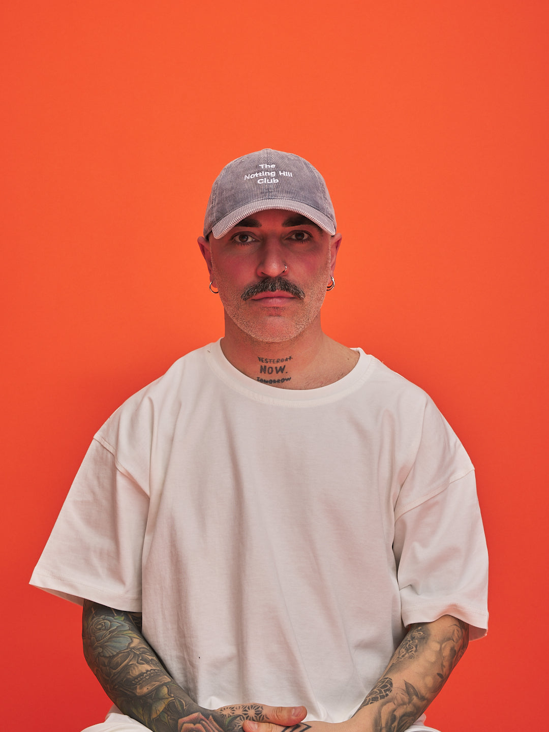 Person wearing a white t-shirt and gray cap against an orange background
