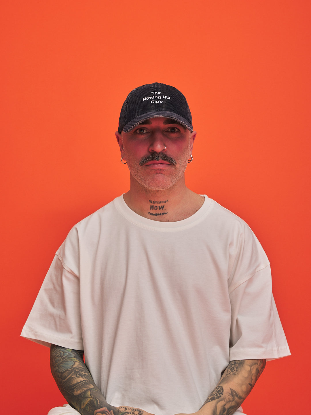 Man wearing a navy cap and white t-shirt against an orange background