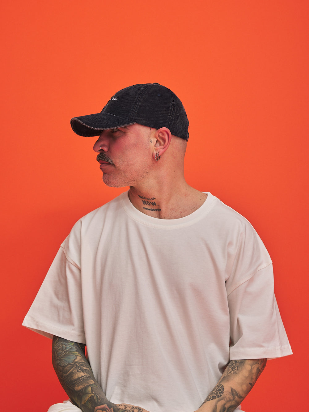 Man wearing a navy cap and white t-shirt against an orange background