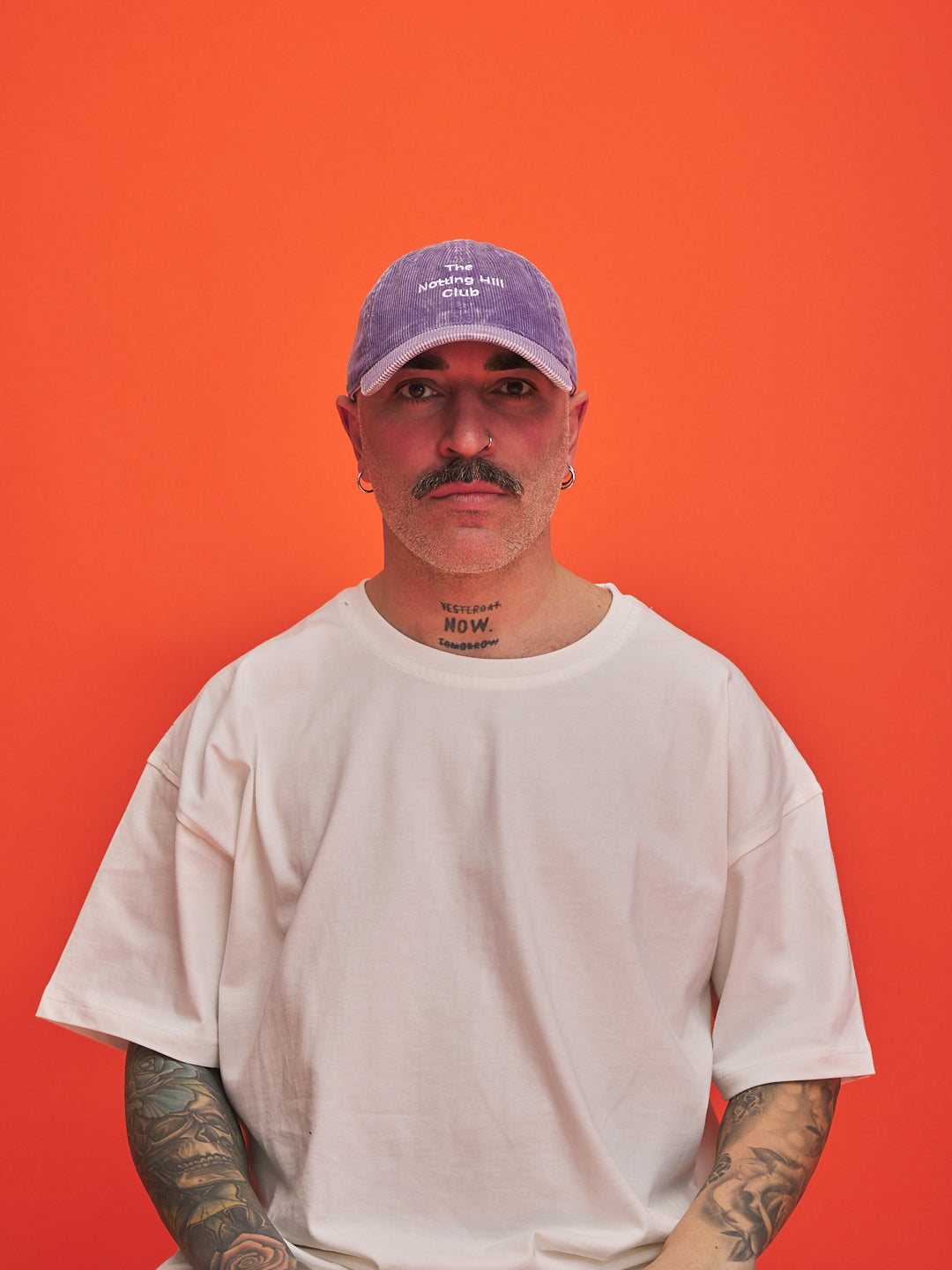 Man wearing a white t-shirt and purple cap against an orange background