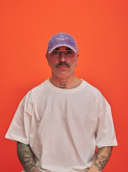 Man wearing a white t-shirt and purple cap against an orange background