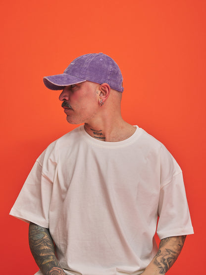 Person wearing a purple cap and white t-shirt against an orange background