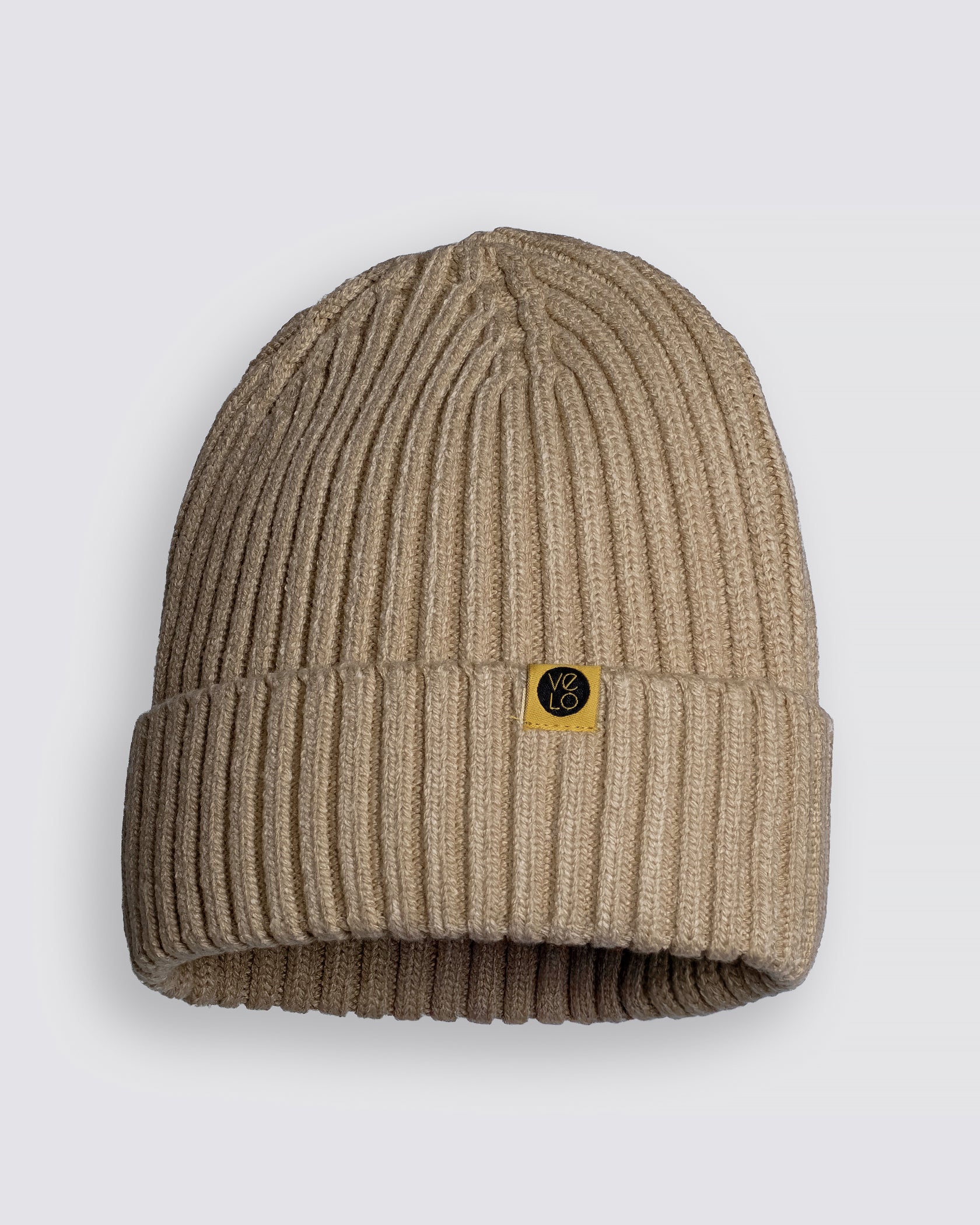 Oat Beige Classic Beanie with a gold logo tag on a light gray background
