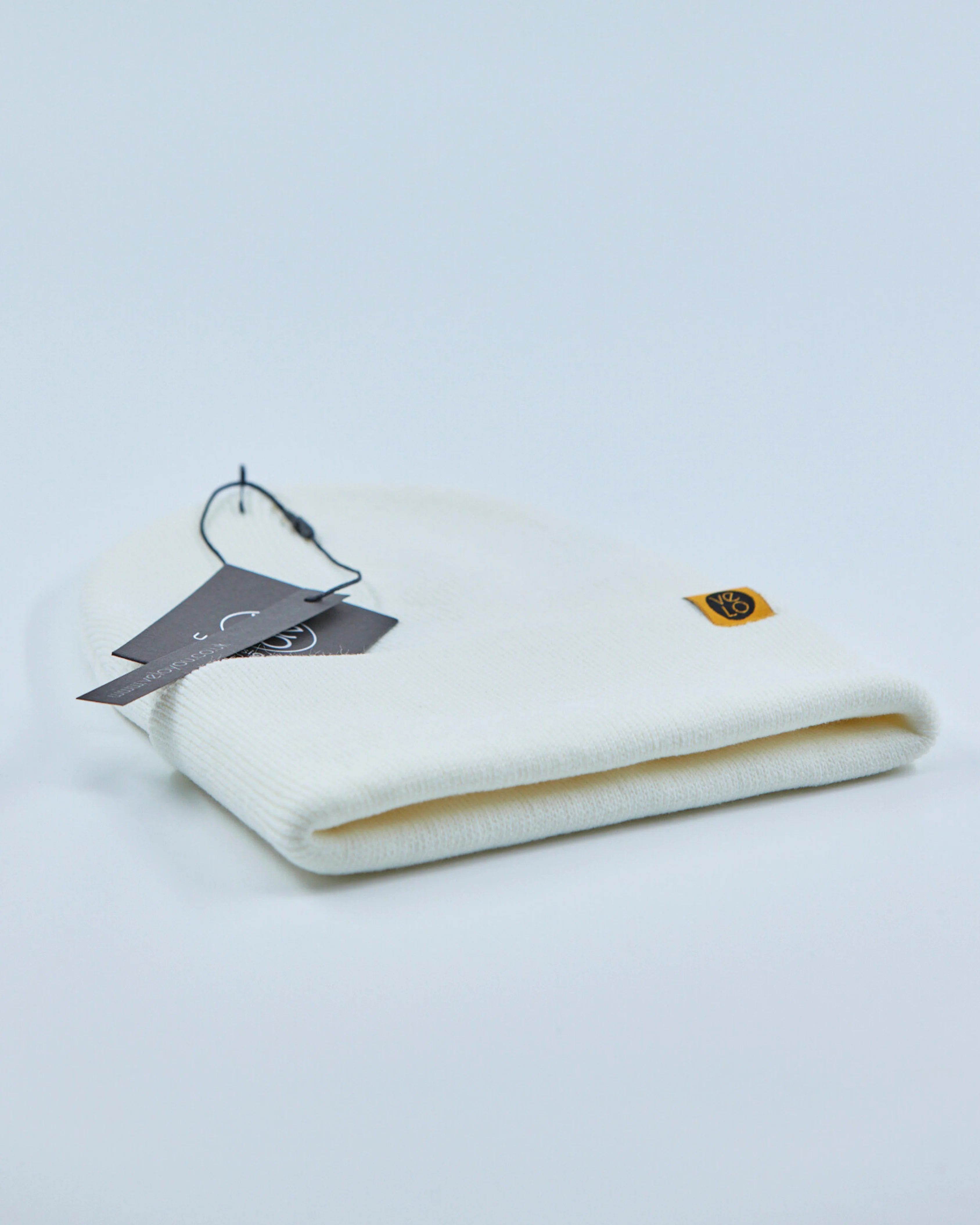 White beanie with a tag and logo on a light gray background