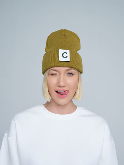 A person wearing olive beanie with 'C' letter patch attached on front on a light gray background