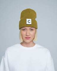 A person wearing olive beanie with 'C' letter patch attached on front on a light gray background