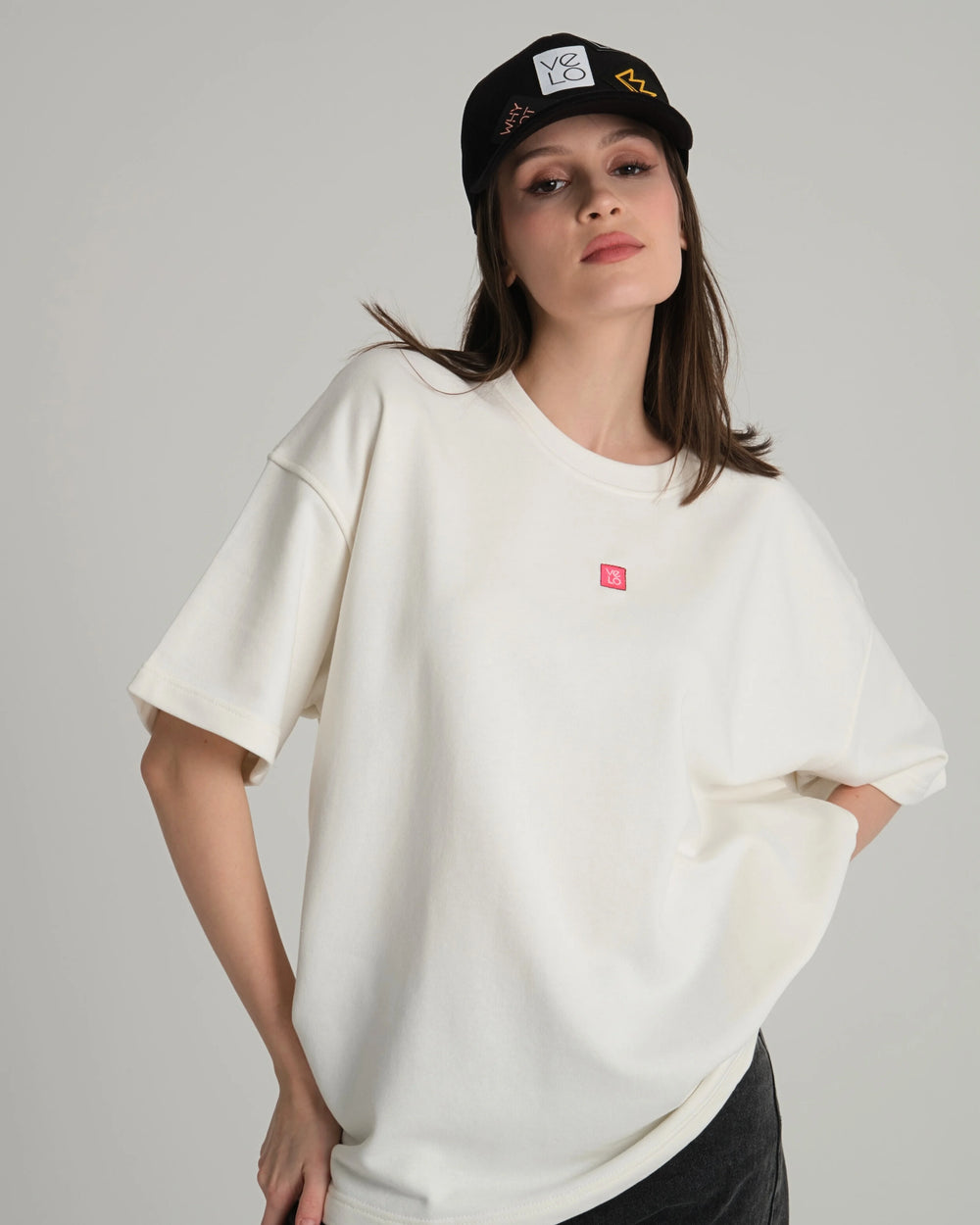 Woman wearing a white oversized shirt and black cap on a gray background