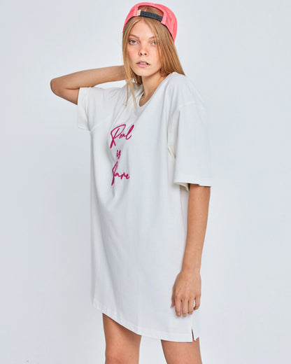 Person wearing a white oversized t-shirt with pink text and a red cap on a light gray background