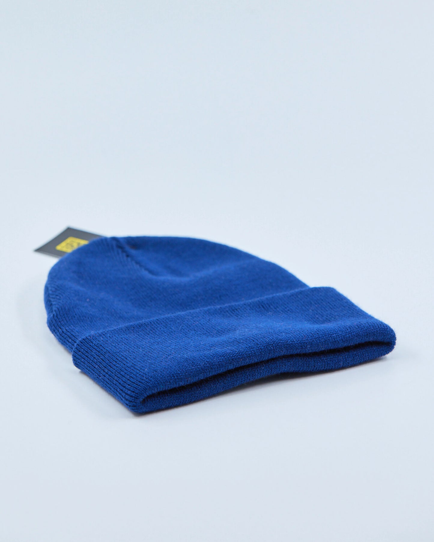 Royal blue beanie with a tag on a light gray background