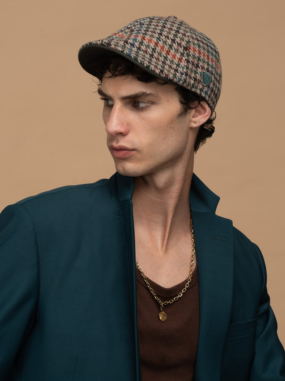 Man wearing Royalty Khaki Casket Hat and dark green jacket against a beige background