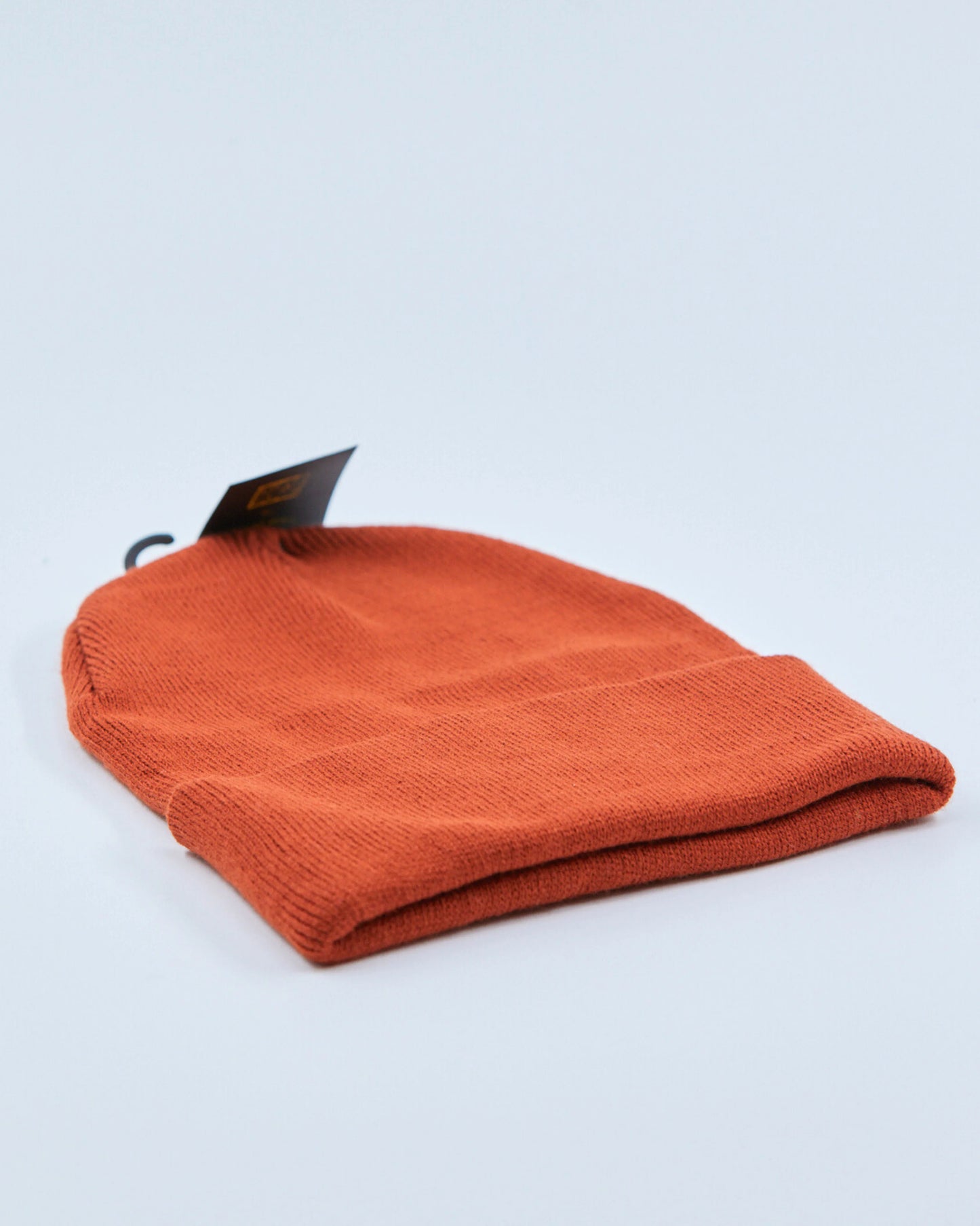 Rust orange beanie with a tag on a light gray background