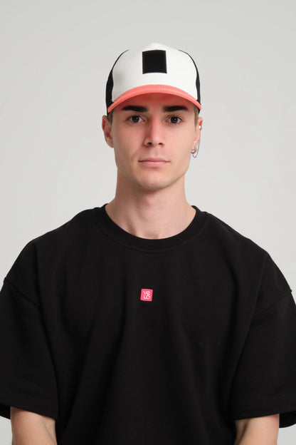 Person wearing a black t-shirt with a small red logo and a white and pink cap on a gray background