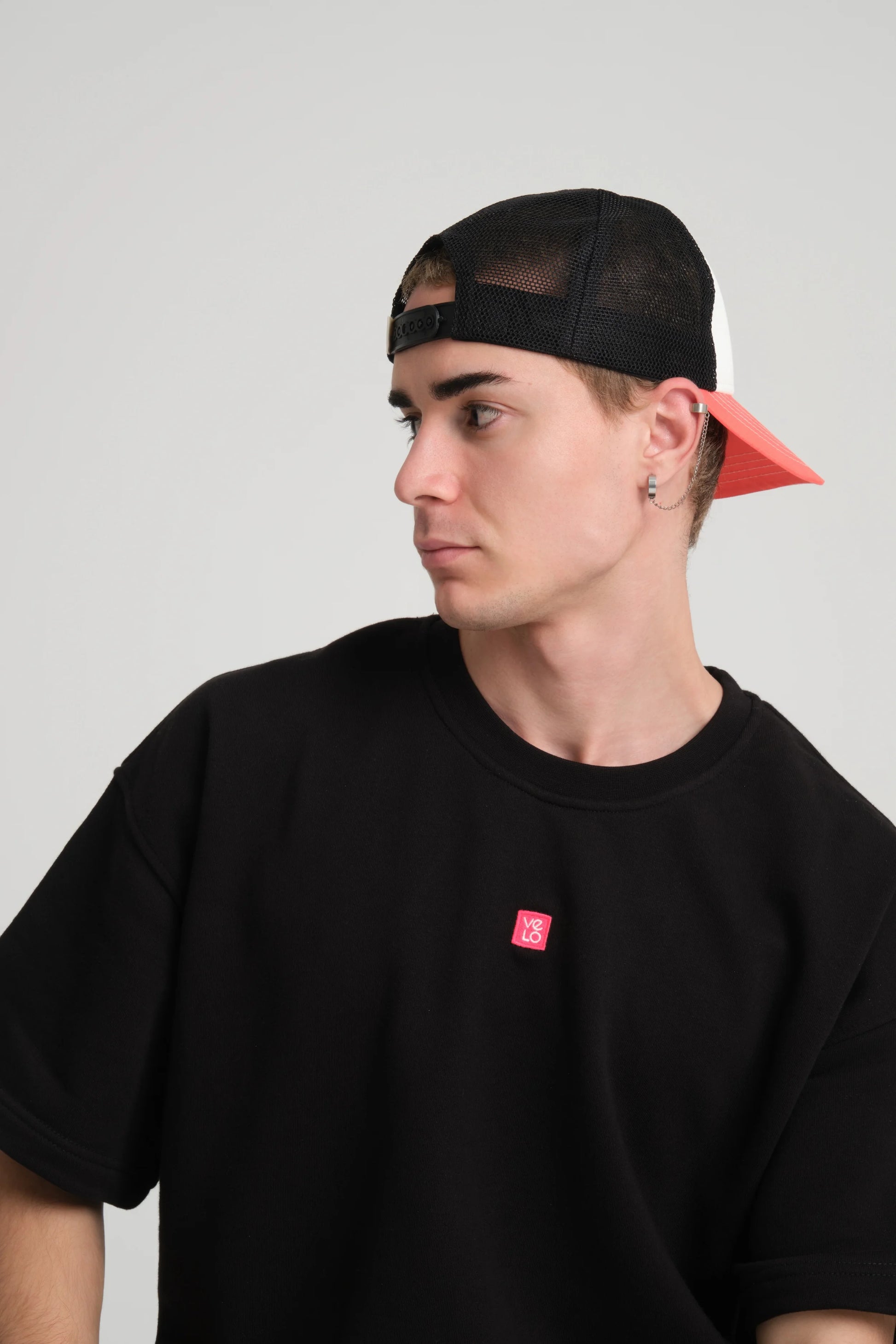 Person wearing a black t-shirt with a red logo and a black cap with a red interior on a light gray background